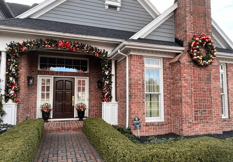 Beautifully decorated brick home entrance with holiday garland and wreath featuring red ribbons and ornaments