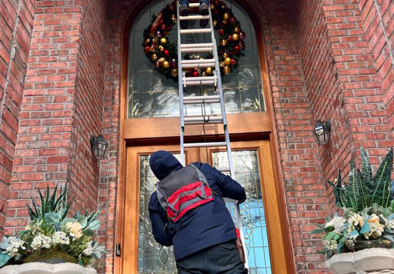 Two workers setting up a large holiday wreath with ornaments above a front door