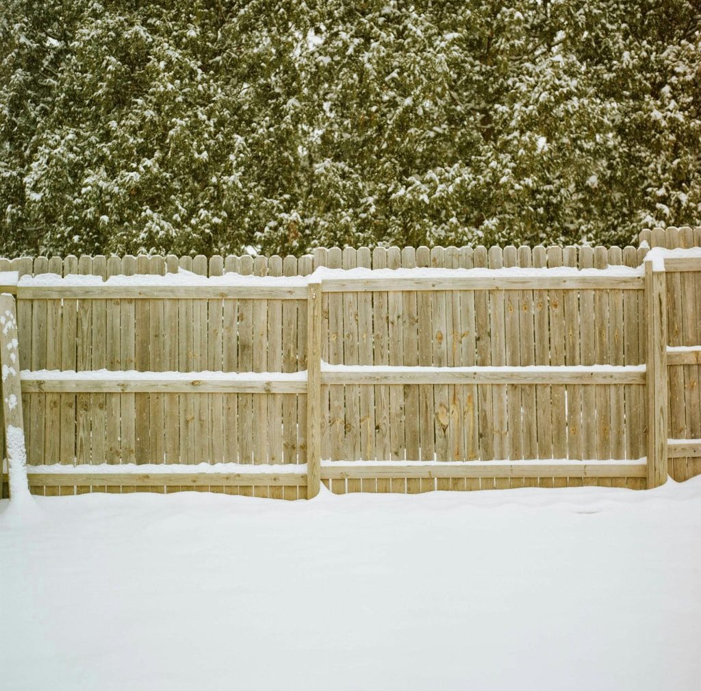 Wooden picket fence covered in snow during winter.